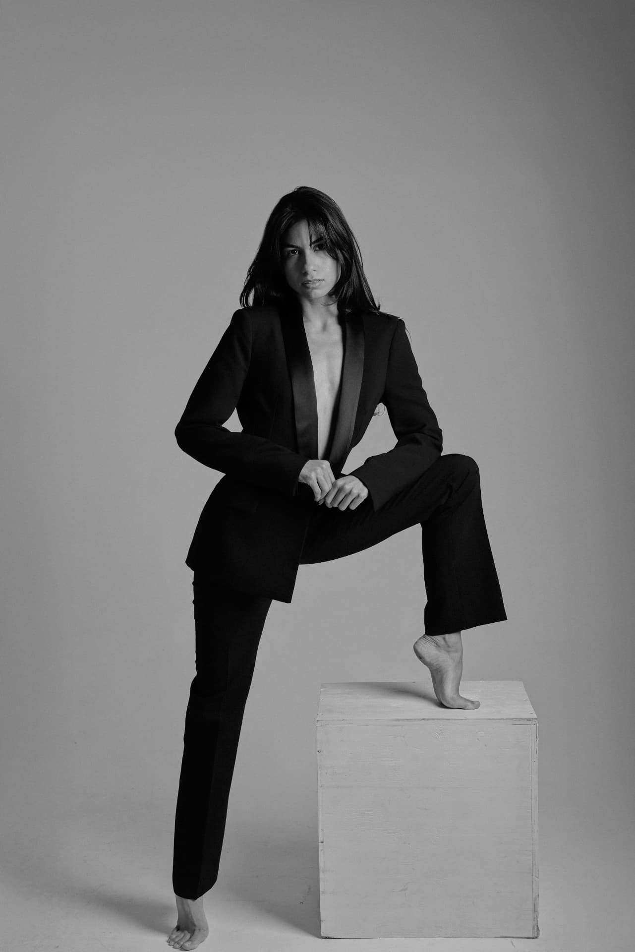 Claudia Cristina en smoking noir, pied posé sur un cube de studio
