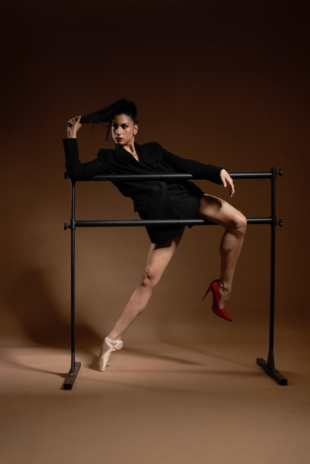 Danseuse en extension sur la barre, lumière chaude et blazer noir